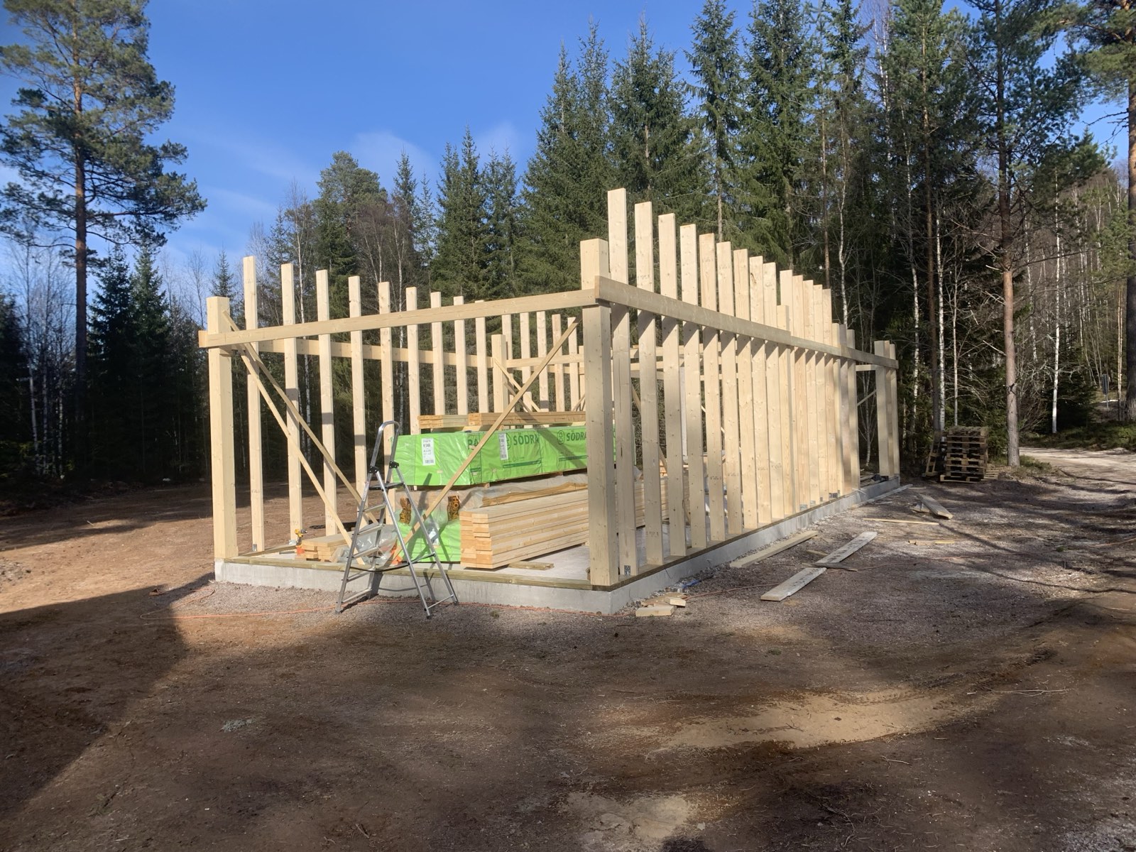A timber-frame outbuilding going up on a concrete slab in the forest